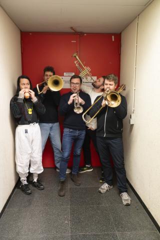 4 darstellende mit Blasinstrumenten vor einer roten Tür, einer mit Spielzeug daneben