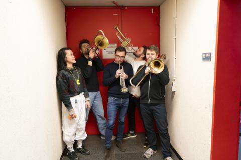 4 darstellende mit Blasinstrumenten vor einer roten Tür, ein weiterer daneben