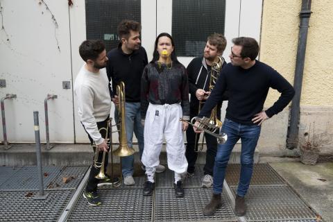 5 Darstellende, 4 mit Blasinstumenten, einer in der Mitte mit Entenschnabel